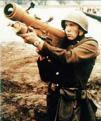 A soldier in a helmet and uniform aims a shoulder-fired missile launcher.